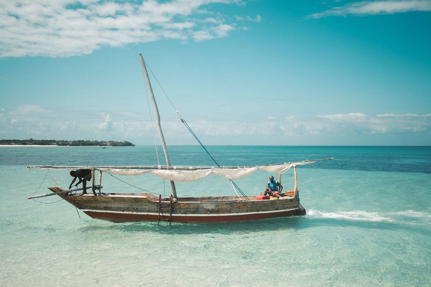 Two fishermen working aboard a small traditional boat in clear inshore water